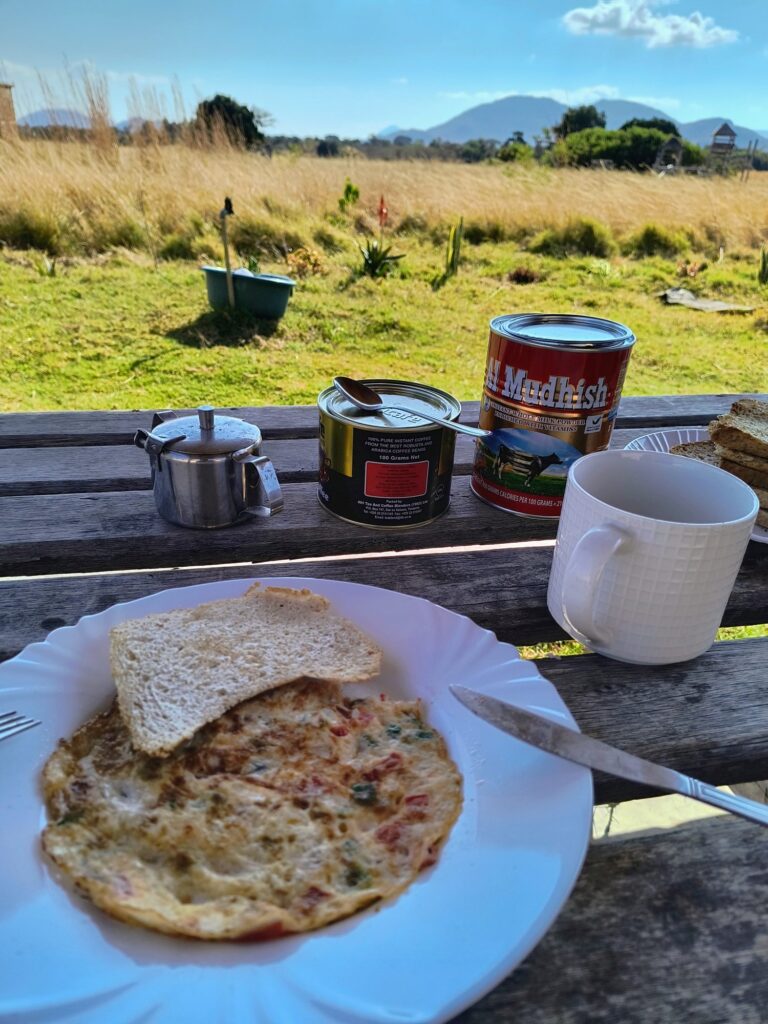 Breakfast with pancakes and fresh fruit on a wooden table, looking out over the grassland and mountains near Iringa